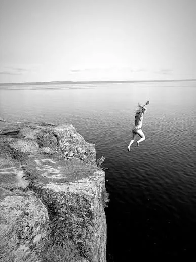 A person leaping from a rocky cliff edge towards the calm sea below